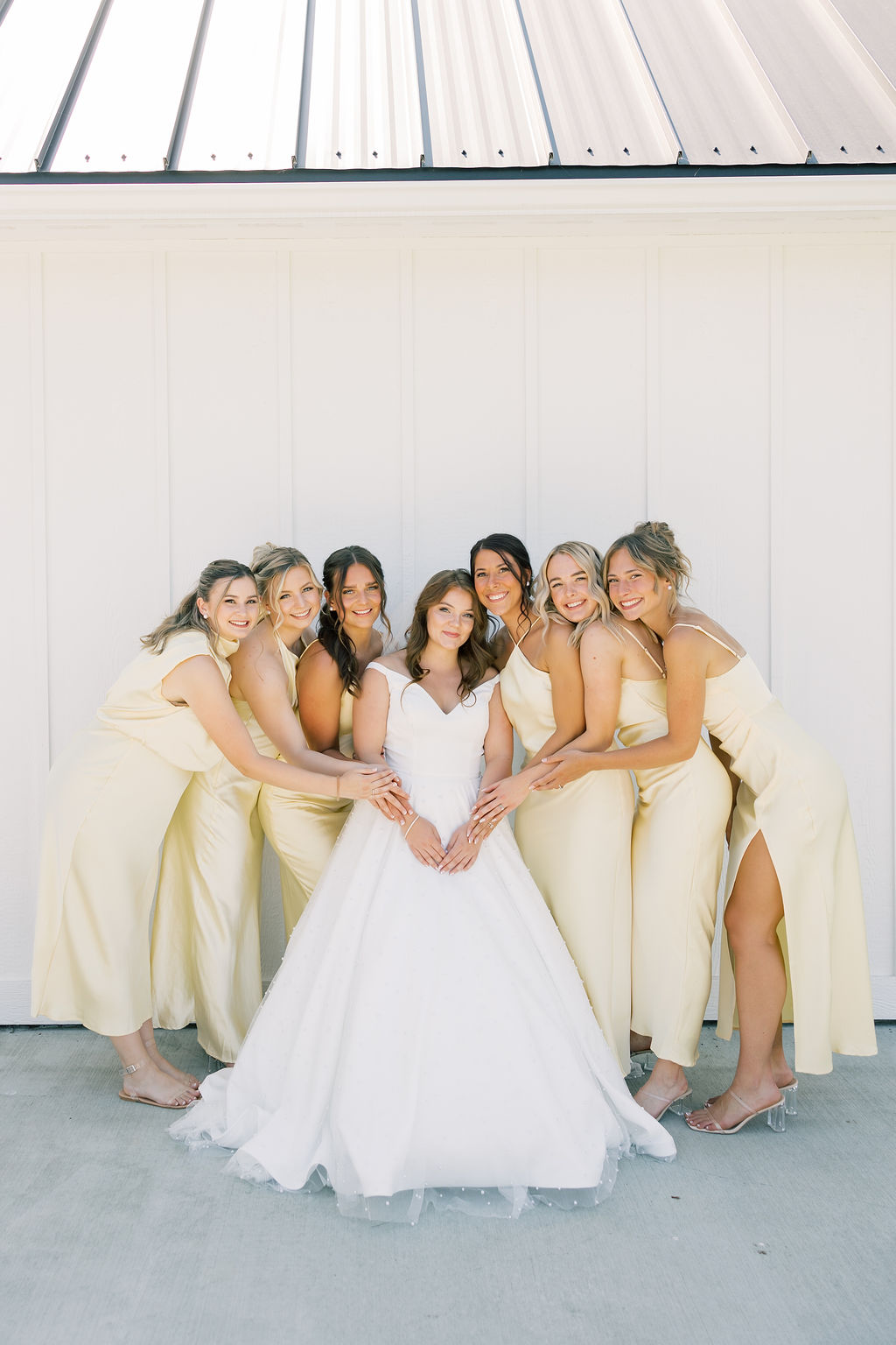 A group of bridesmaids hug the bride in gold dresses on a porch