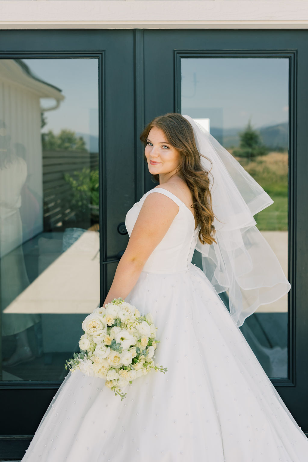 A bride smiles over her shoulder while holding her bouquet