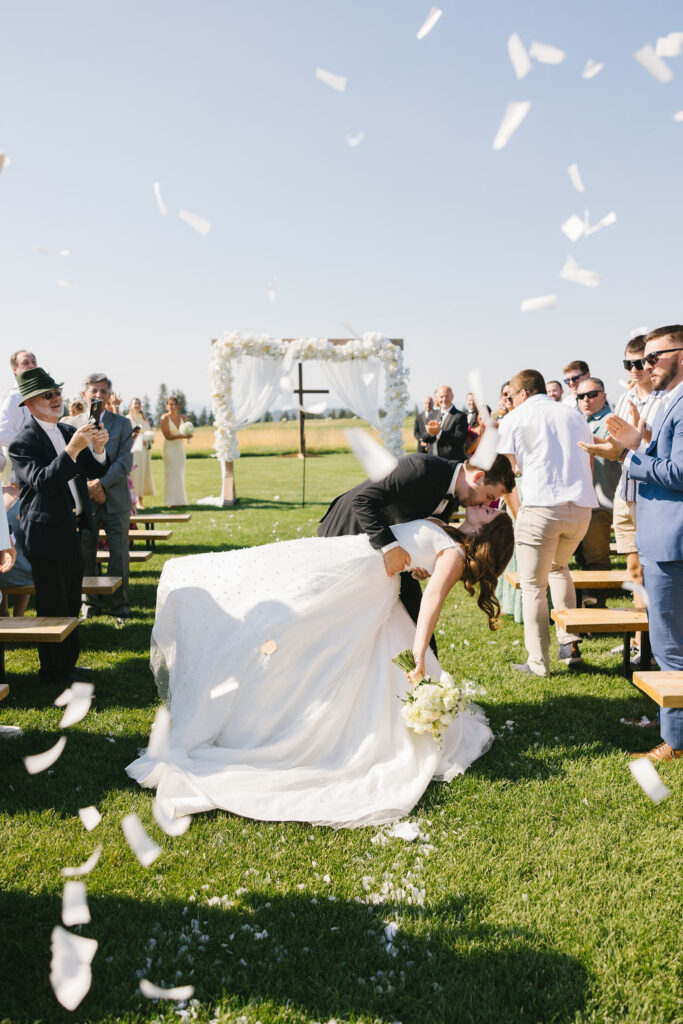 A groom dips his bride for a kiss in the aisle under a shower of confetti at farmhouse on green bluff