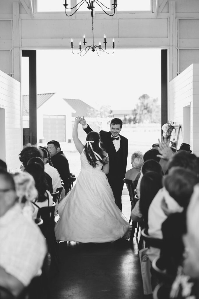 Newlyweds dance through the reception hall aisle under a chandelier at farmhouse on green bluff