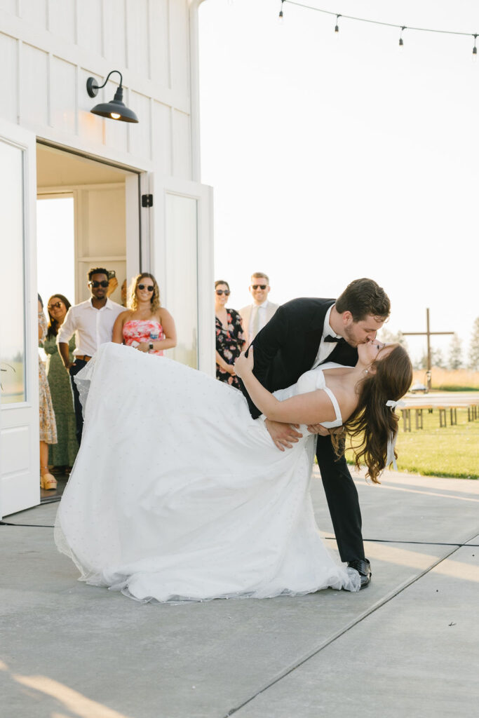 Newlyweds dip and kiss while dancing under market lights at sunset at their farmhouse on green bluff reception