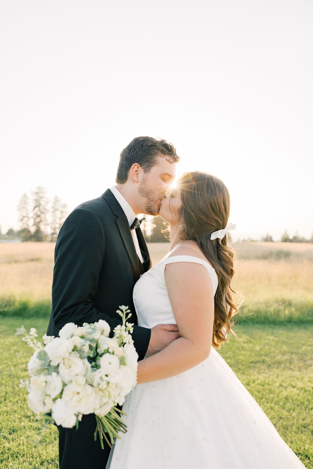 Newlyweds kiss at sunset in the pasture at farmhouse on green bluff