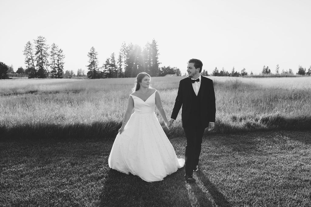 Newlyweds walk and hold hands through a pasture at their farmhouse on green bluff wedding