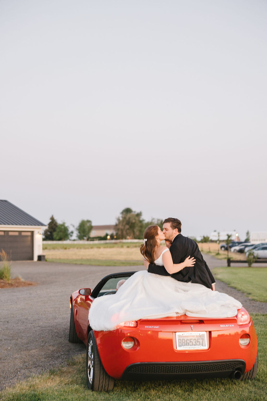 Newlyweds kiss while sitting in the back of a red covertable