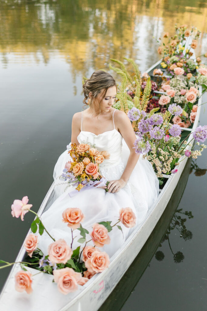 A bride gazes down her shoulder while sitting in a canoe