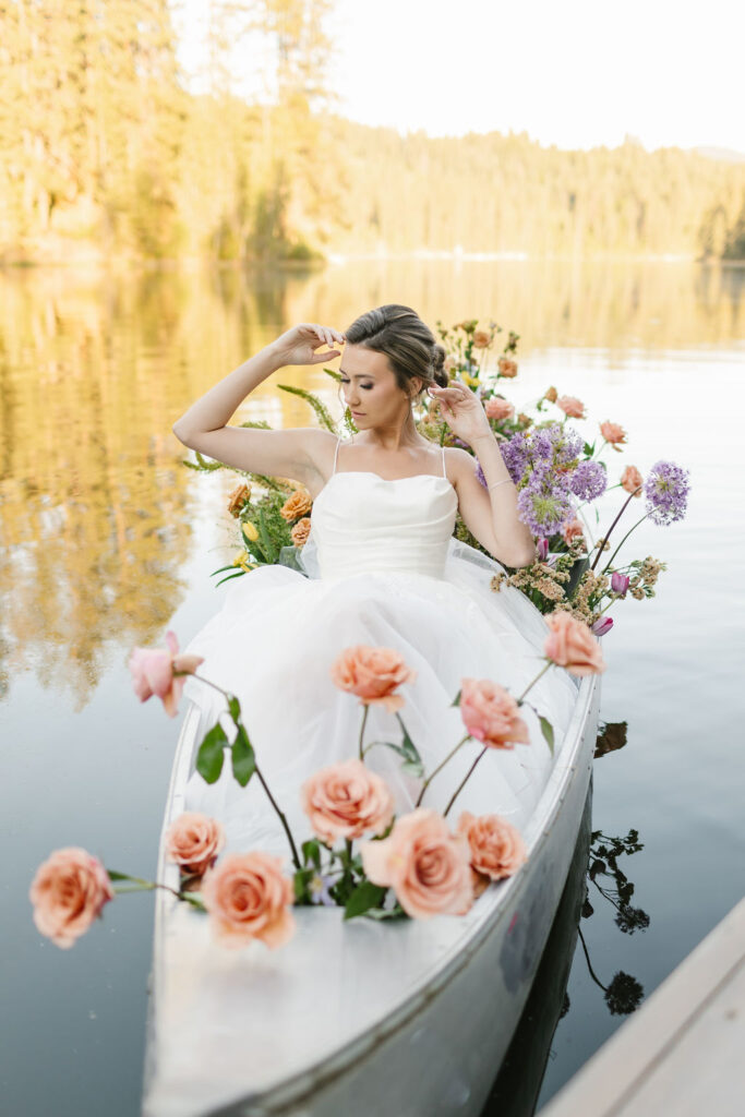 A bride lounges surrounded by flowers in a canoe in a lake at sunset