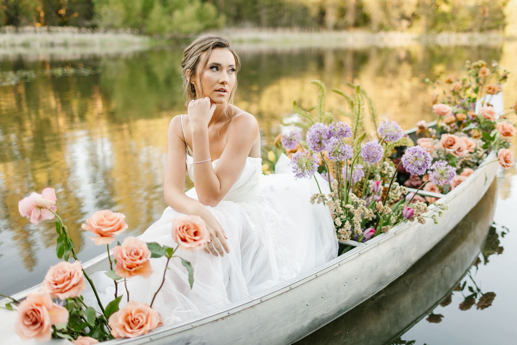 A bride leans on her hand while sitting in a canoe filled with flowers at one of the lakefront wedding venues coeur d'alene