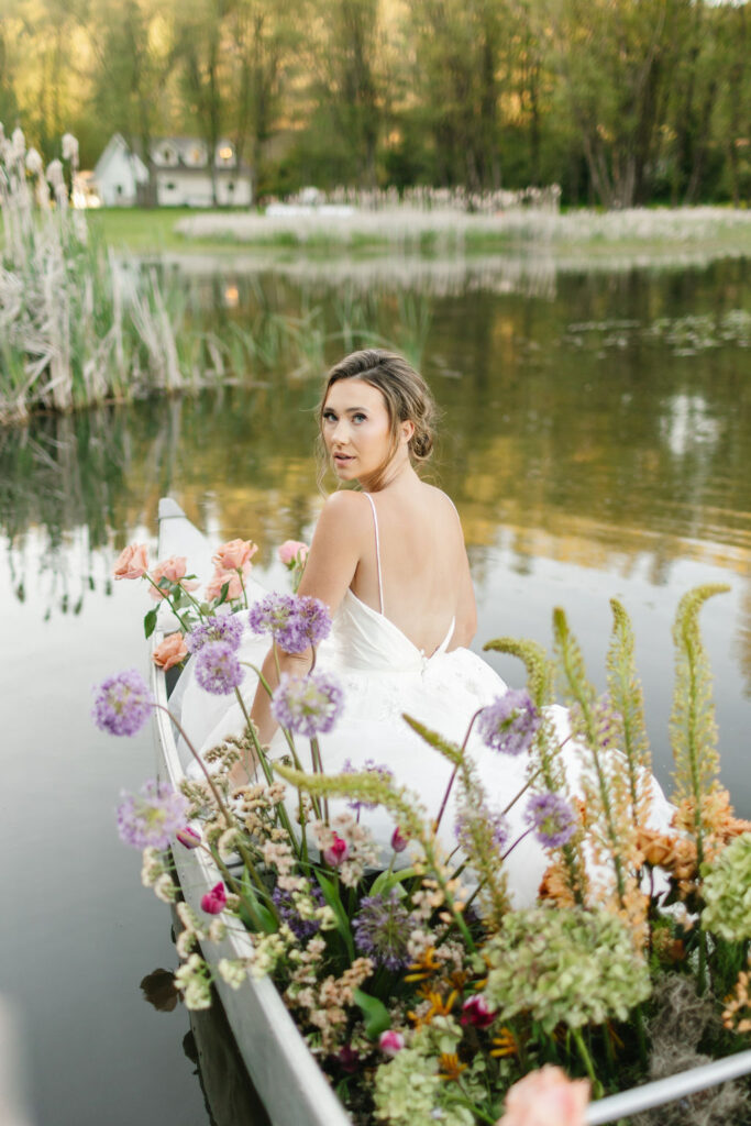 A bride looks over her shoulder while sitting in a canoe on a lake at lakefront wedding venues coeur d'alene