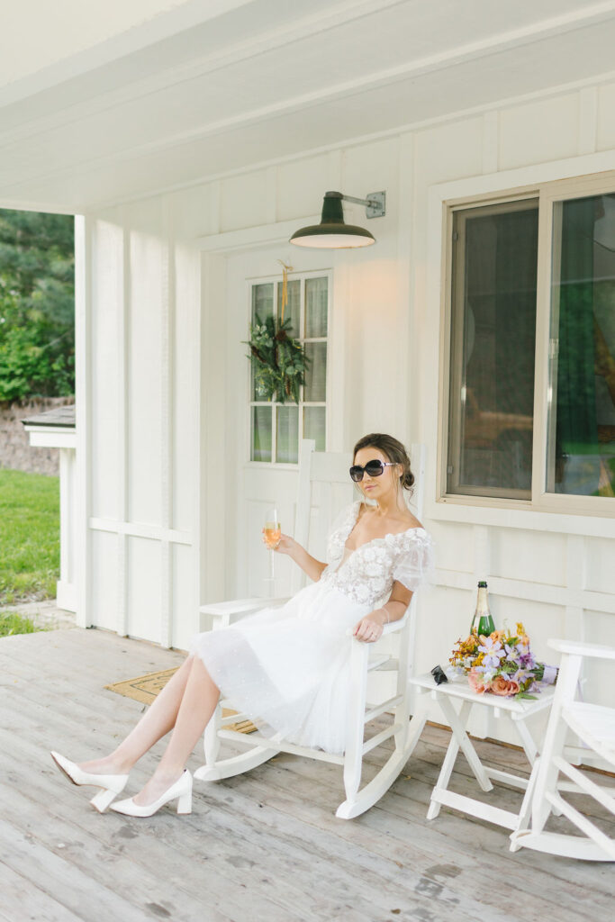 A bride lounges on a porch of one of the lakefront wedding venues coeur d'alene drinking champagne in a rocking chair