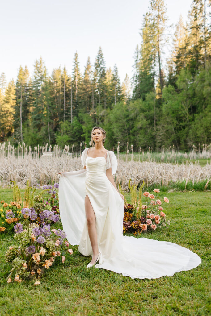 A bride holds her train open while walking by flower displays at her ceremony location