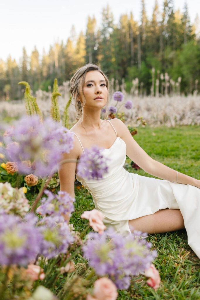 A bride sits in a lawn in the grass with some purple flowers at one of the lakefront wedding venues coeur d'alene