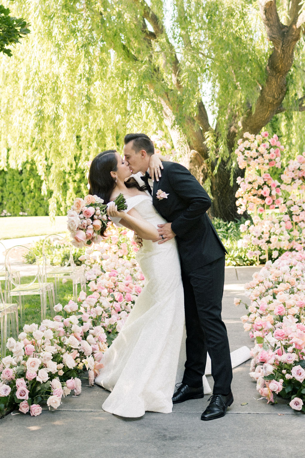 Newlyweds kiss in the aisle lined with pink roses at their promise garden pasco wedding ceremony