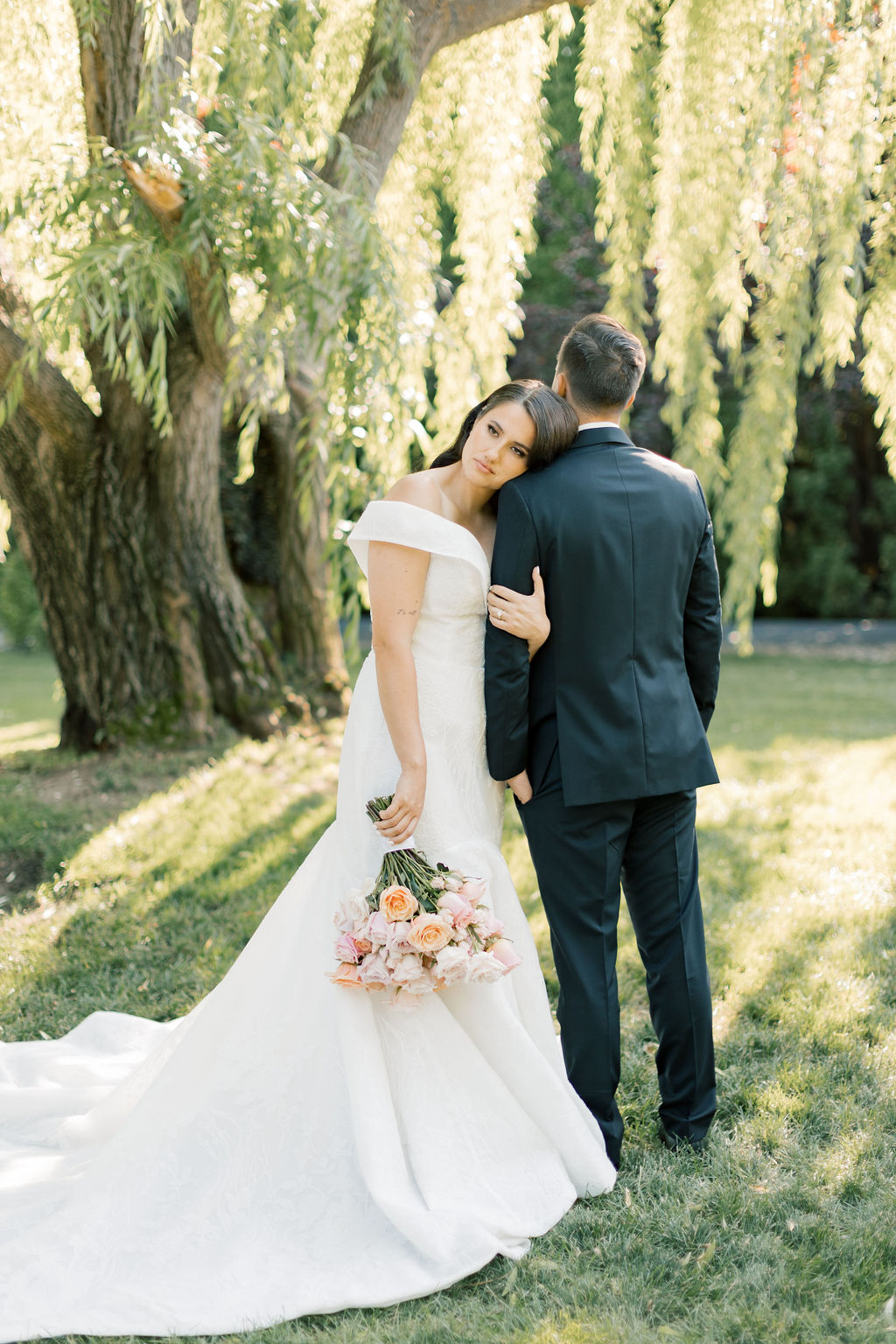 A bride leans on the shoulder of her groom under the willow tree at promise garden pasco