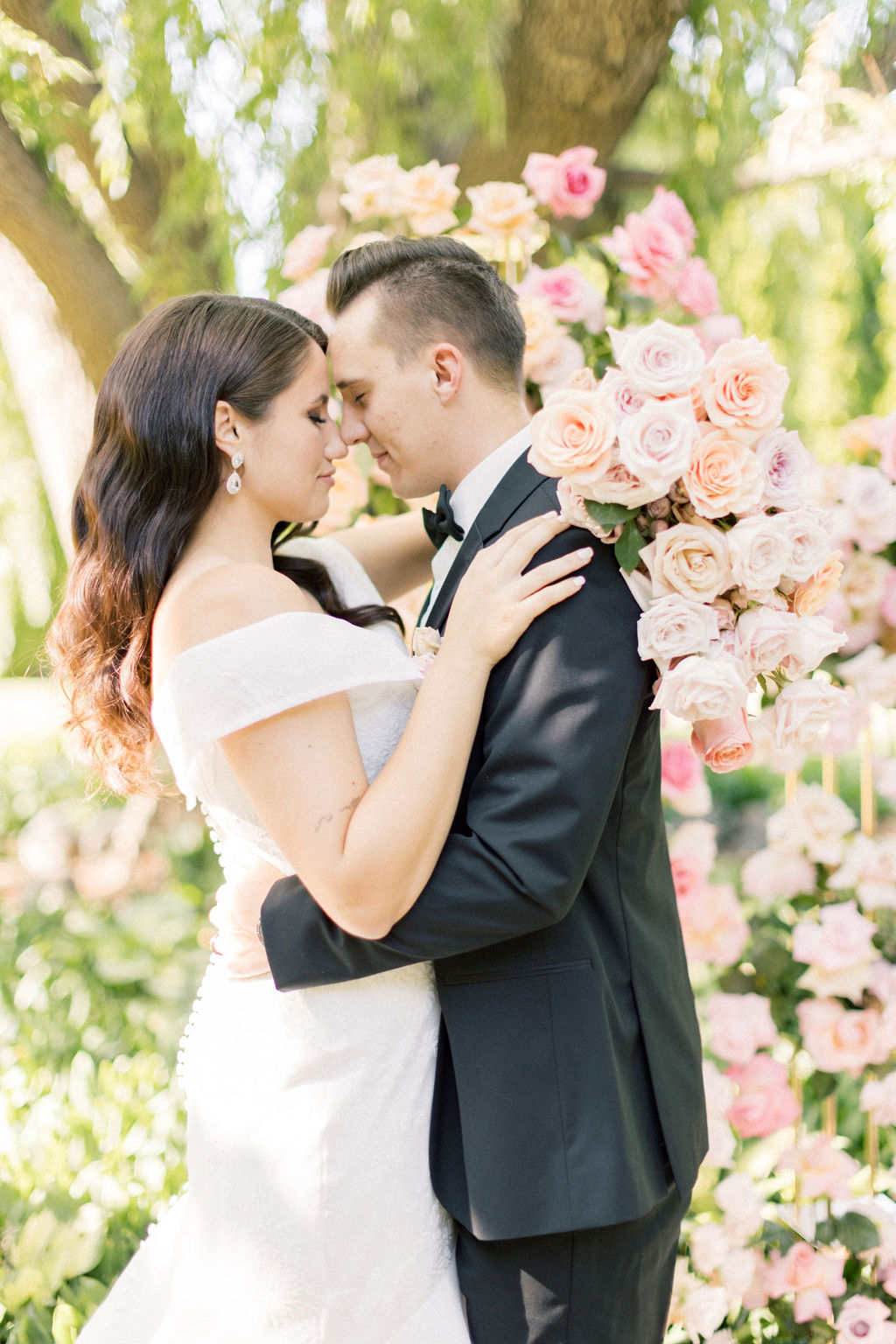 A bride and groom hug touching noses in a garden of pink roses at promise garden pasco