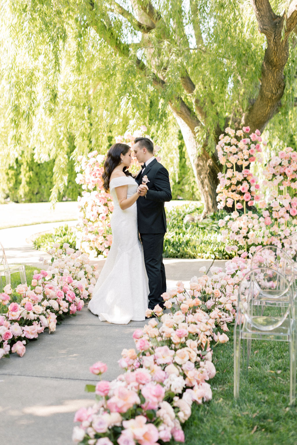 Newlyweds hold hands and dance intimately in the sidewalk under a large willow tree