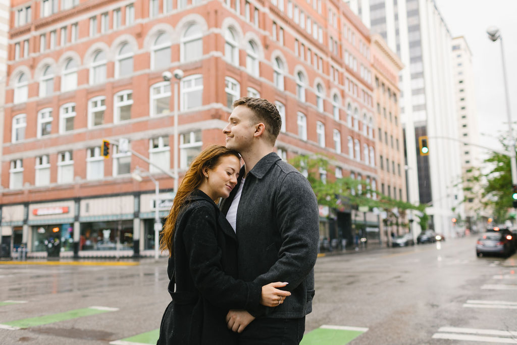 An image taken by a spokane engagement photographer of a couple snuggling on a street corner on a rainy day