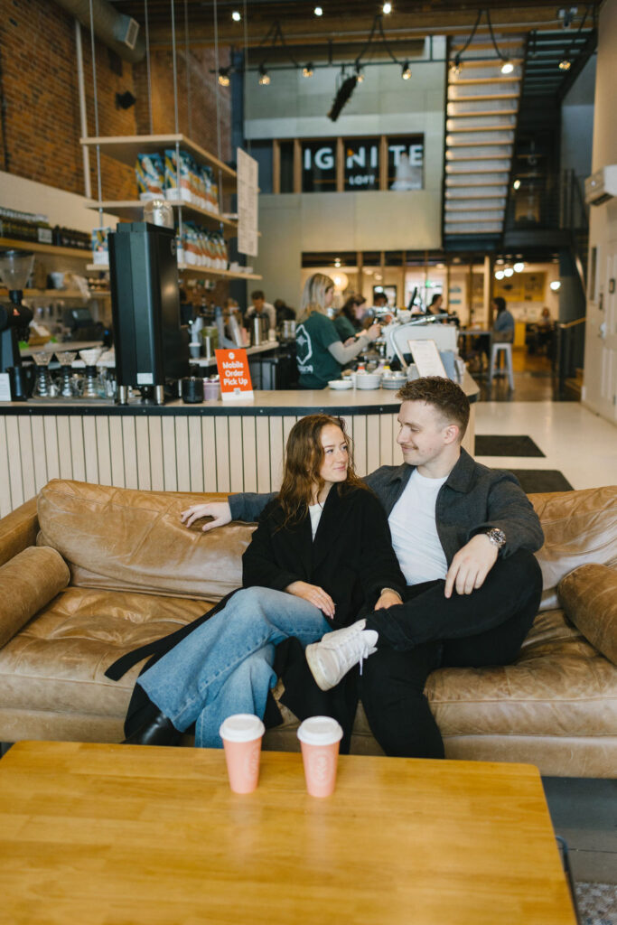 A couple snuggles on a leather couch in a coffee shop