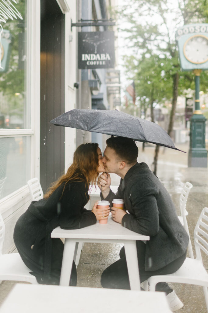 An image from a spokane engagement photographer of a couple kissing at a cafe table under an umbrella