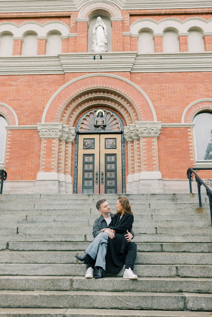 A woman sits in the lap of her fiancee on the steps of a church for a spokane engagement photographer