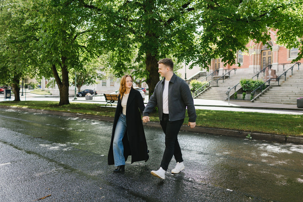 A couple holds hands while crossing a street towards their spokane engagement photographer