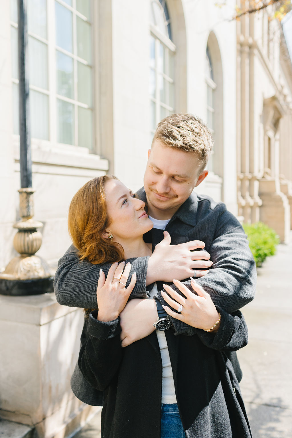 A happy couple snuggles on a downtown street while smiling at each other