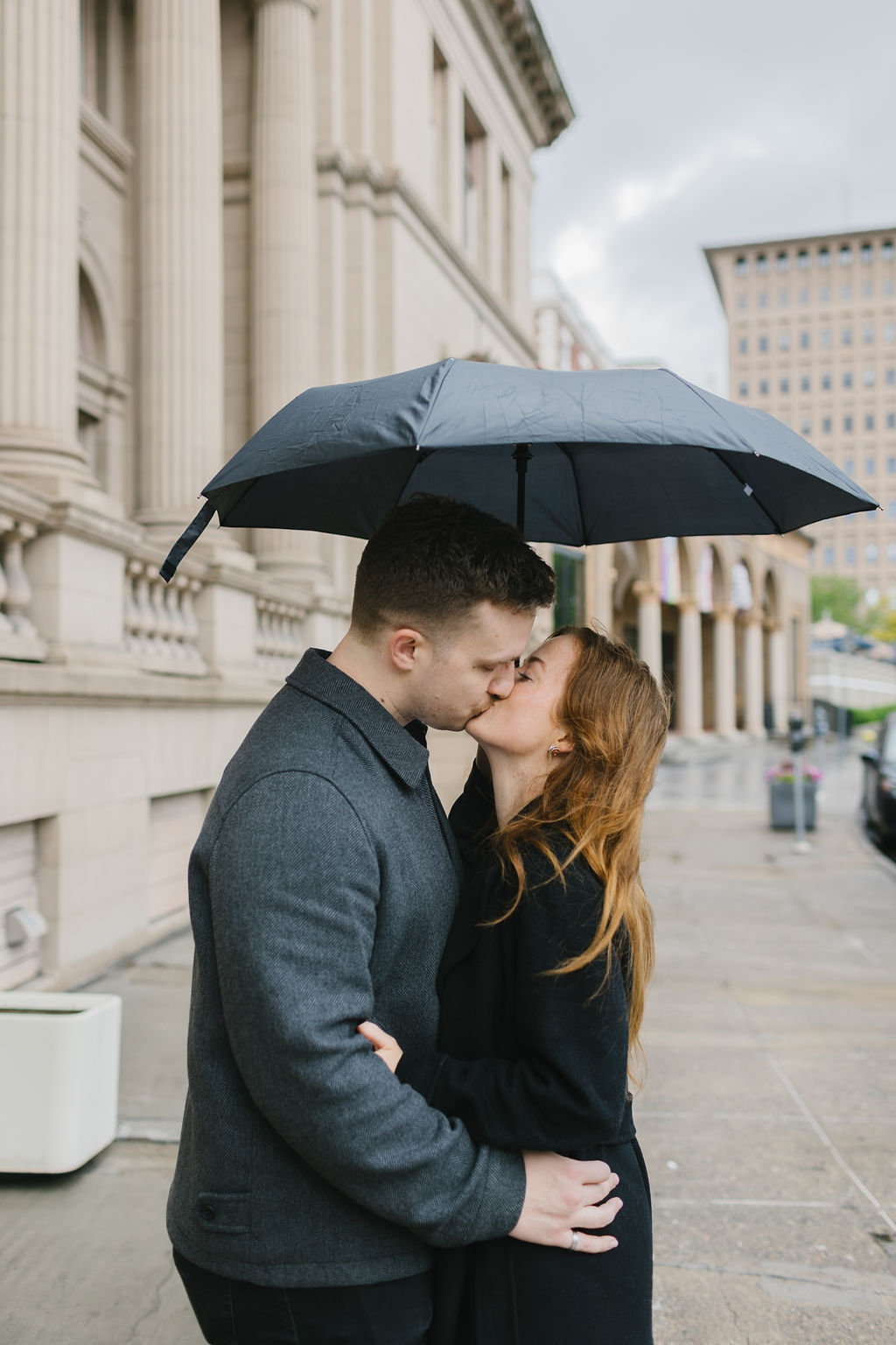 A couple kisses under a small umbrella on a rainy day in downtown with their spokane engagement photographer