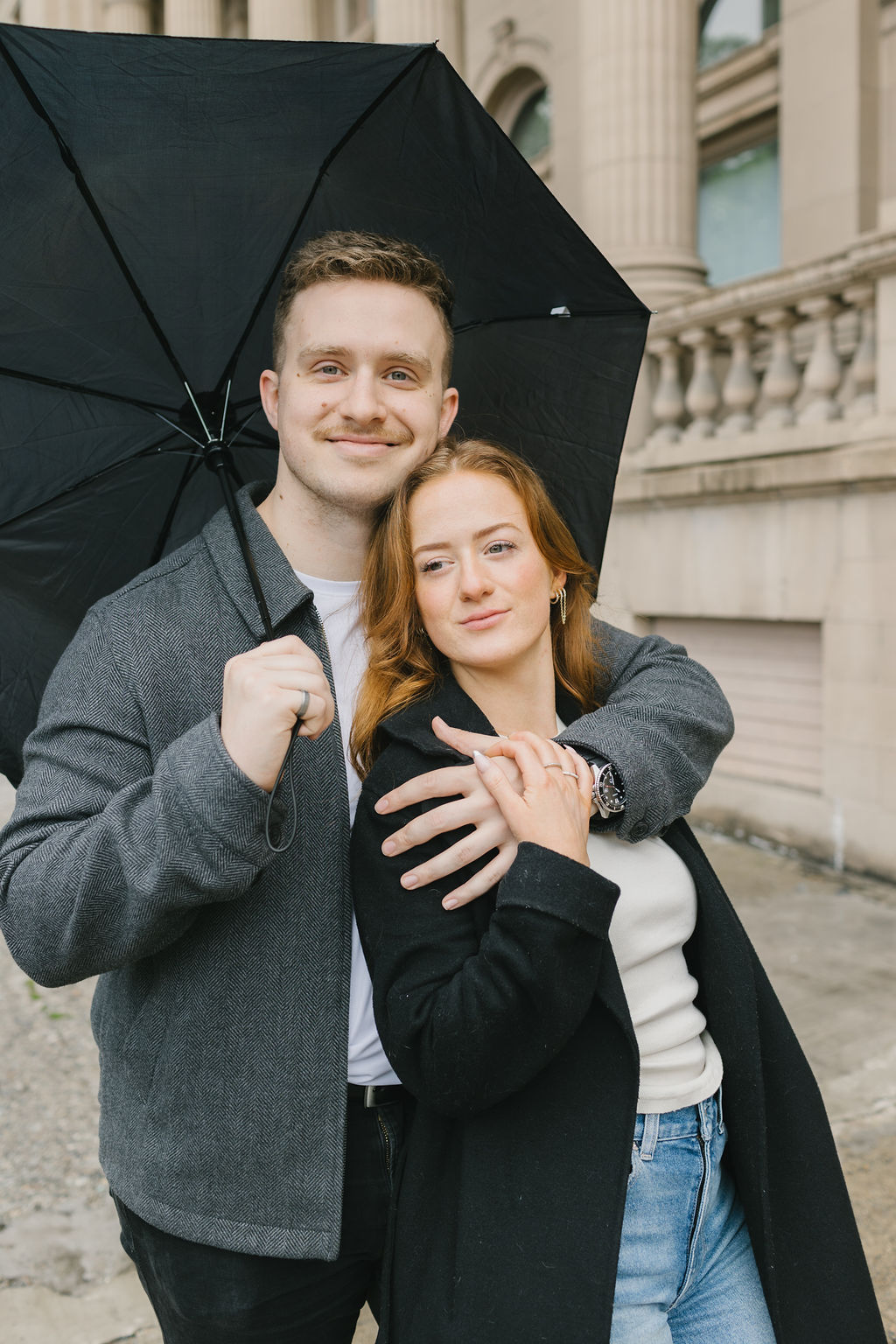 A happy couple stands under an umbrella snuggling in downtown