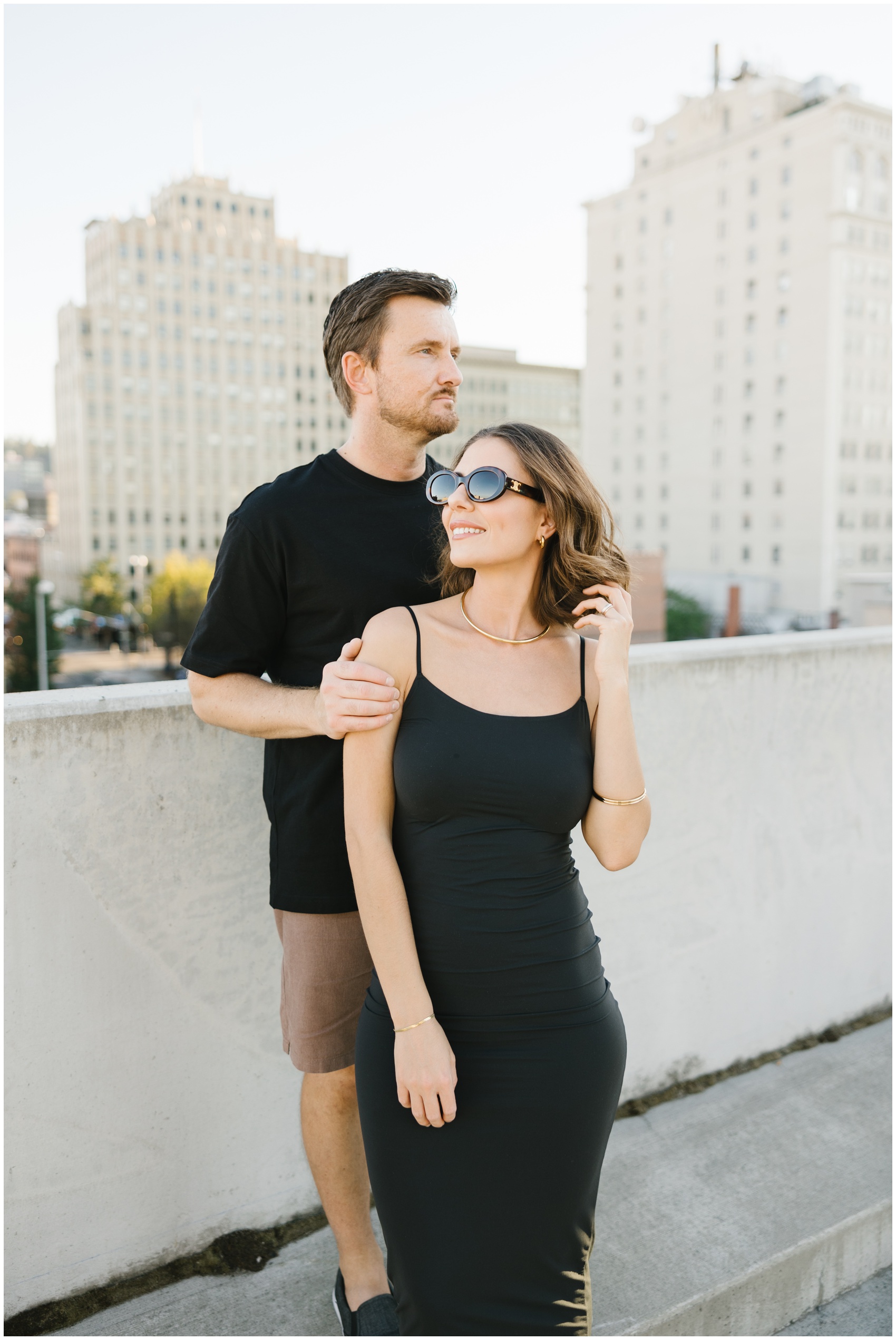 A woman stands with her fiancee both in black on a downtown rooftop