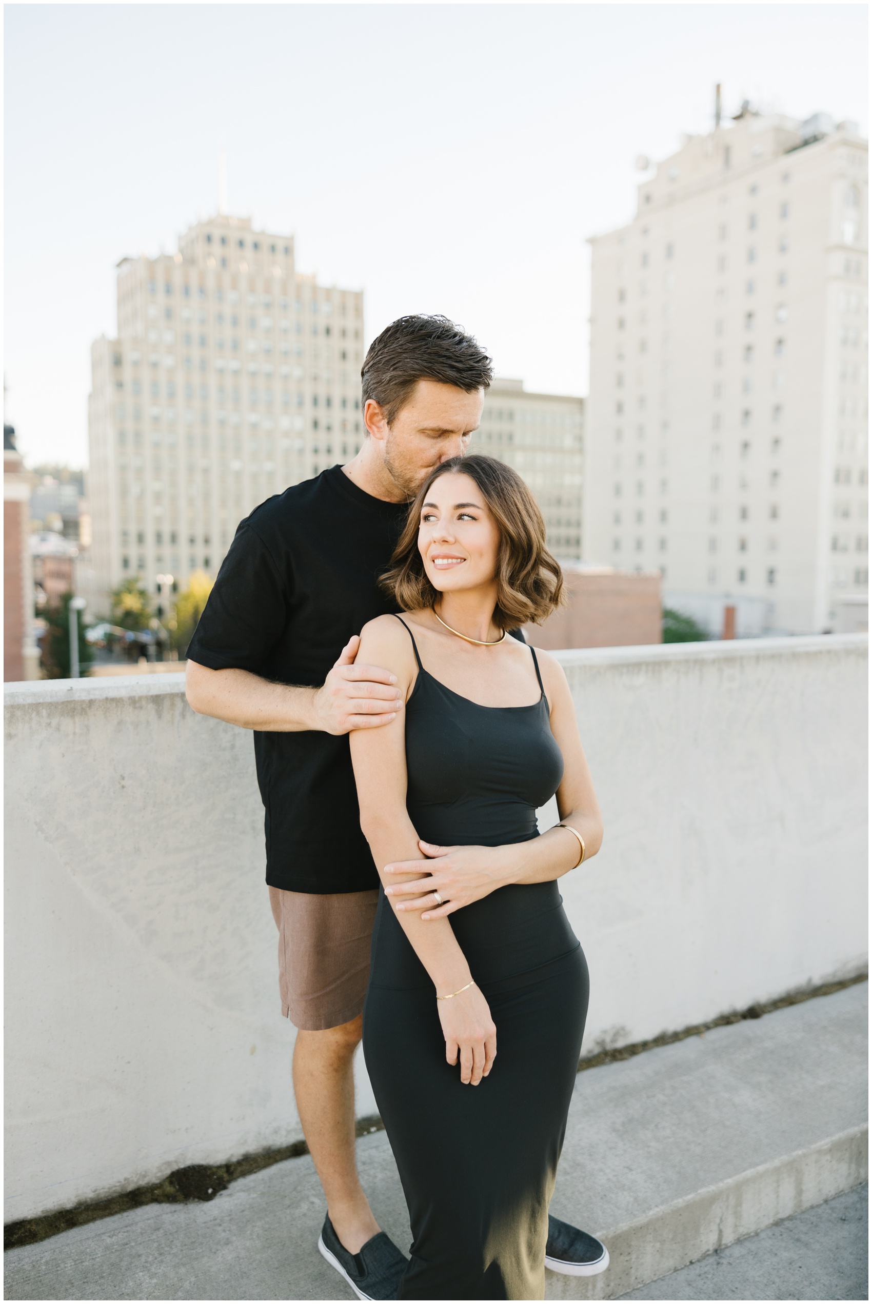 A man kisses the head of his fiancee as they stand on a roof