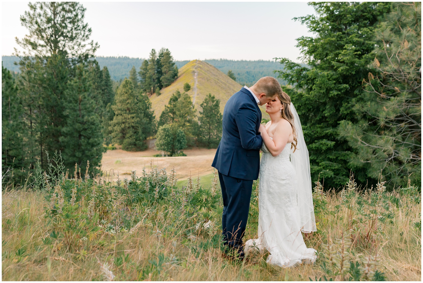 Newlyweds lean in for an intimate kiss on a hilltop overlook in tall grass at their suncadia resort wedding