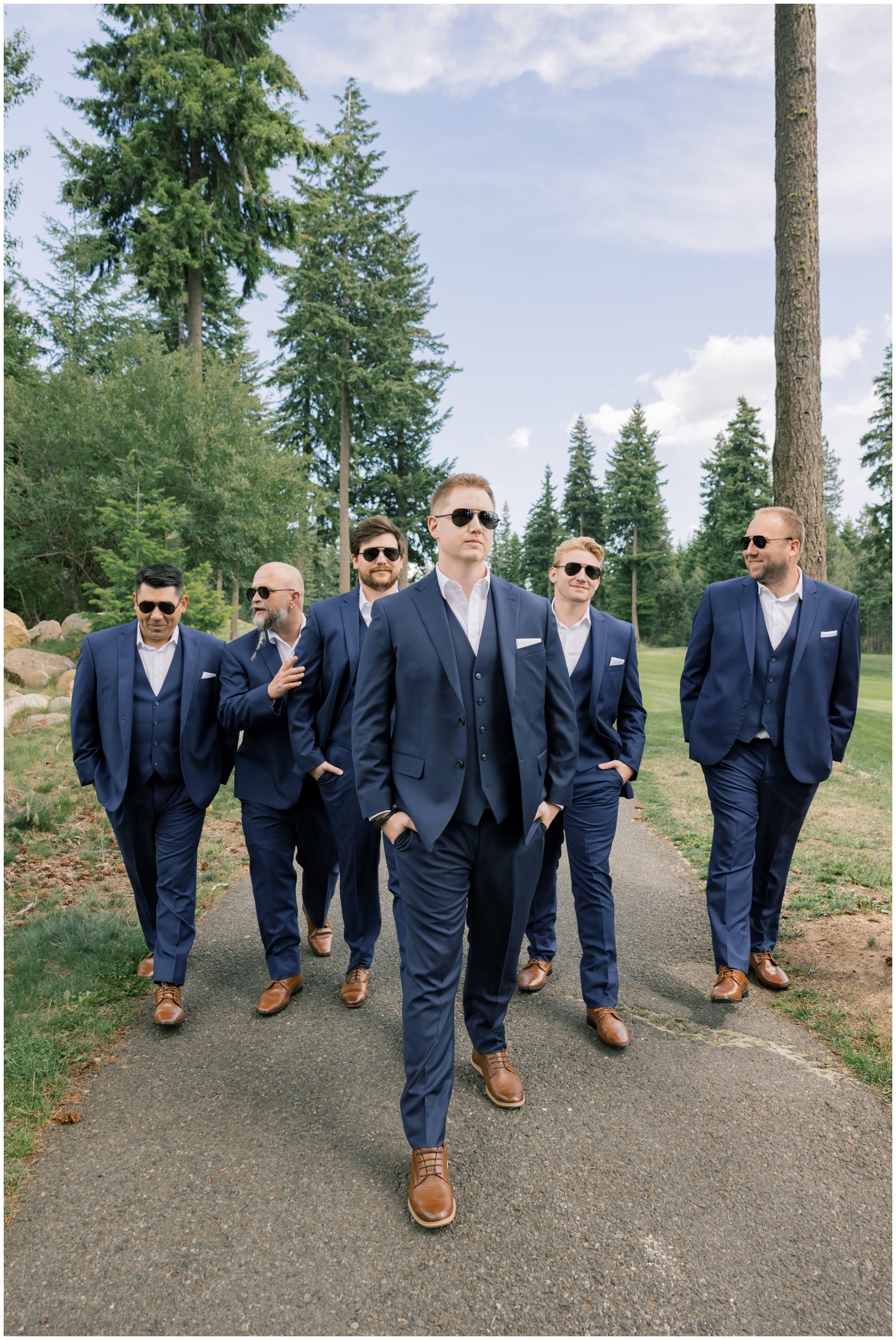 A groom walks with hands in pockets and sunglasses with his matching groomsmen