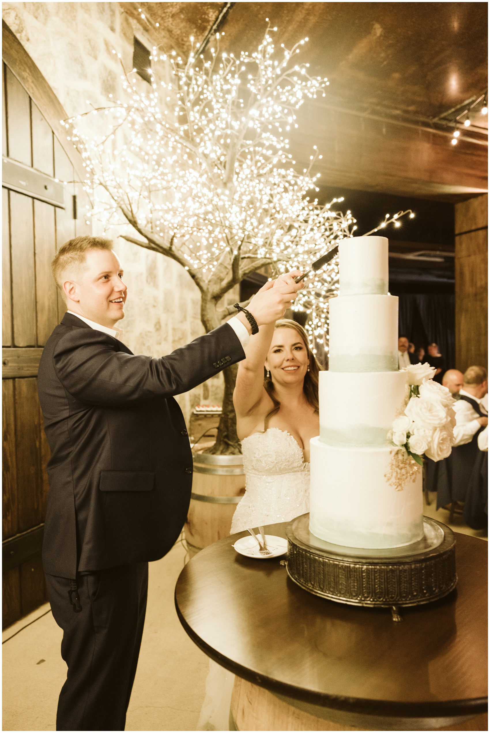 A bride and groom reach high to cut their four tier cake at their swiftwater cellars wedding