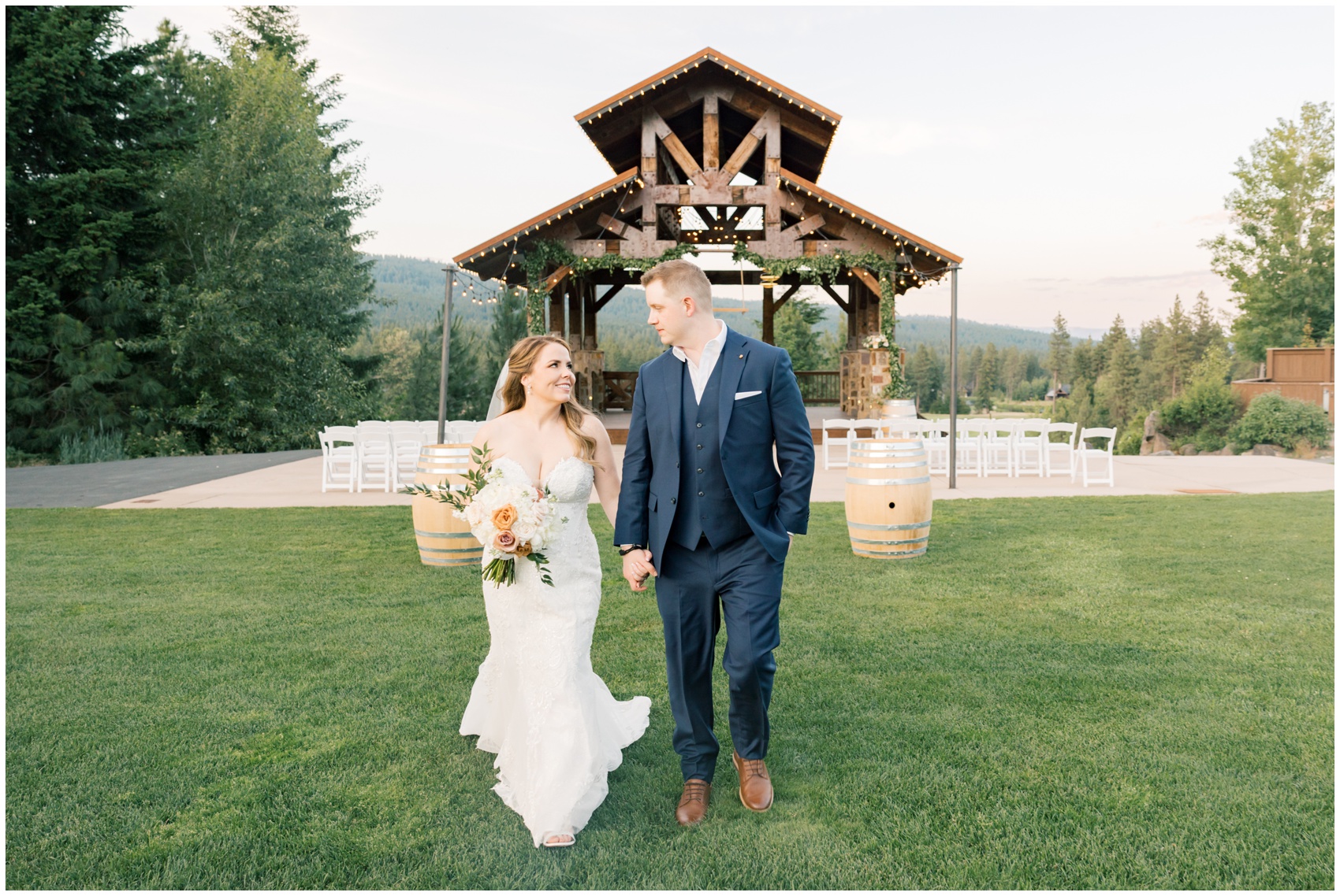 Newlyweds walk hand in hand through the lawn with mountains in the background