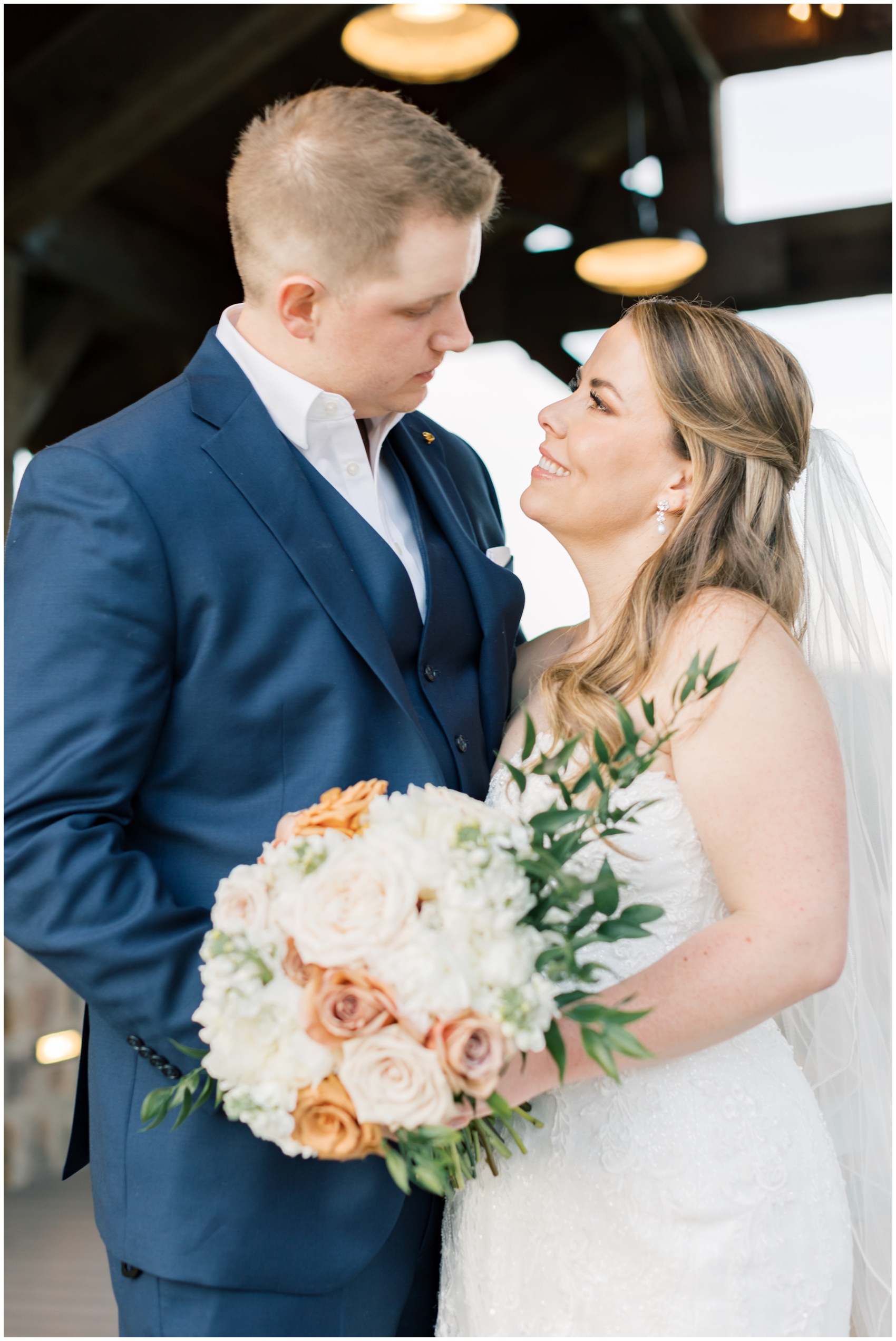 A bride smiles up to her groom as they stand together holding the white and pink bouquet