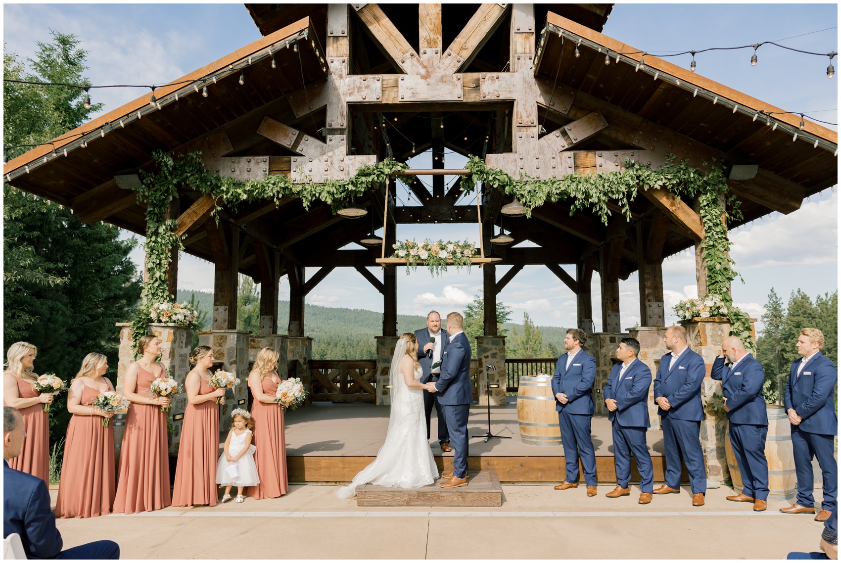 Newlyweds stand at the altar holding hands framed by their wedding party at their outside swiftwater cellars wedding ceremony