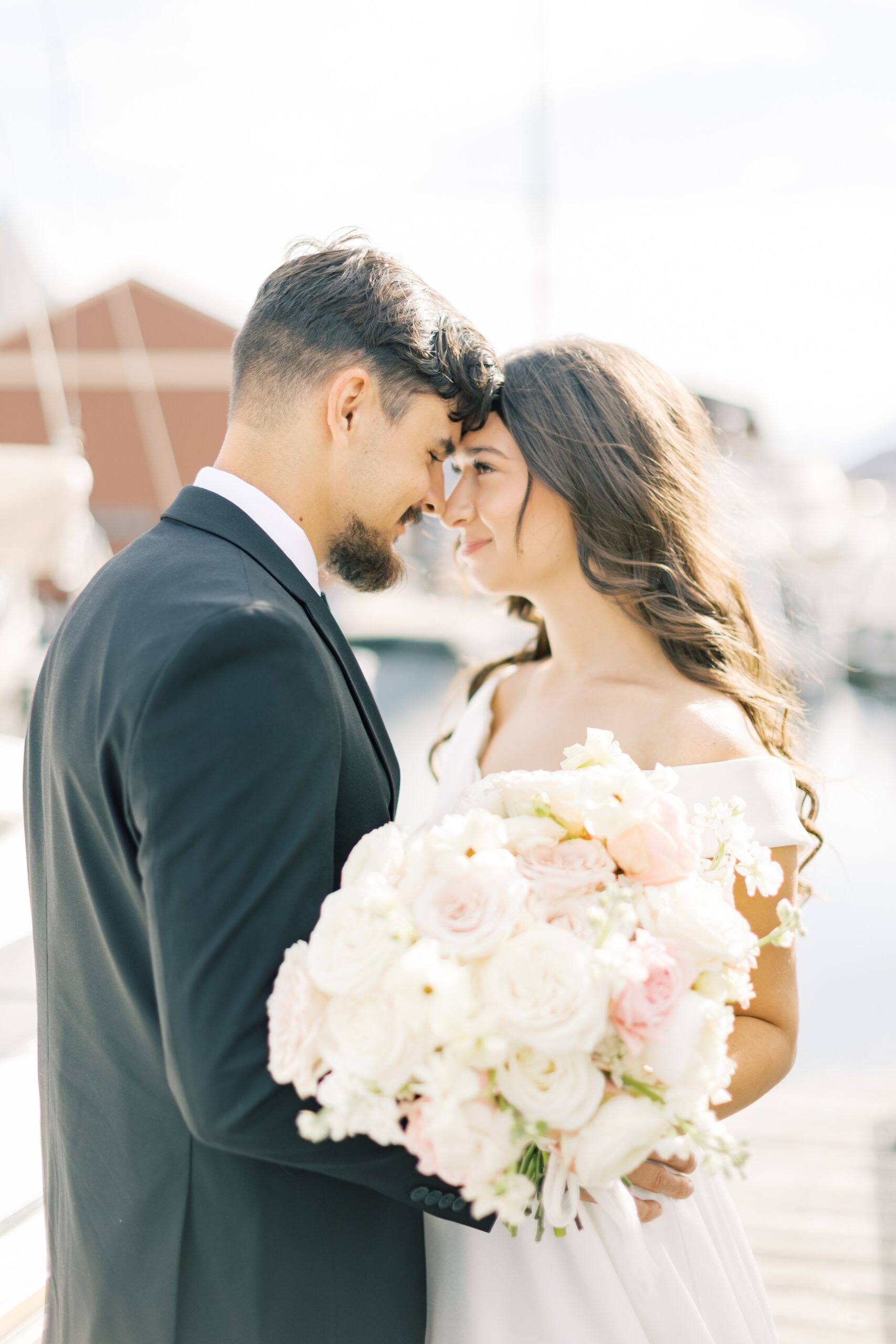 Newlyweds smile and touch foreheads while standing on a dock in a marina