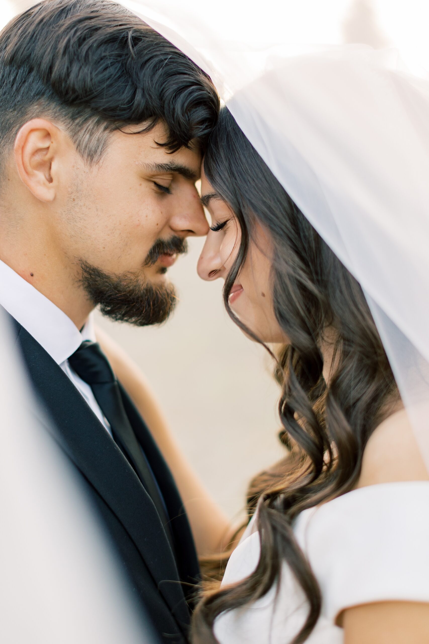 Newlyweds snuggle under the veil touching foreheads at sunset at one of the beautiful Hayden Lake wedding venues