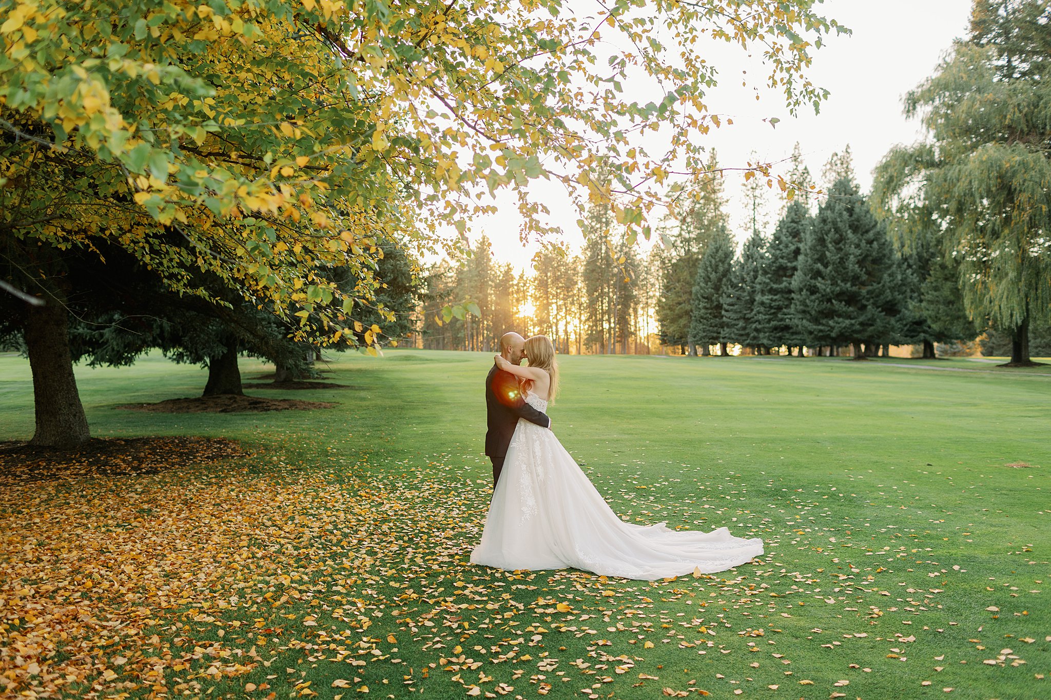 Newlyweds hug and cuddle while touching noses under a fall tree at sunset in an open field at the Kalispel Country Club Wedding venue