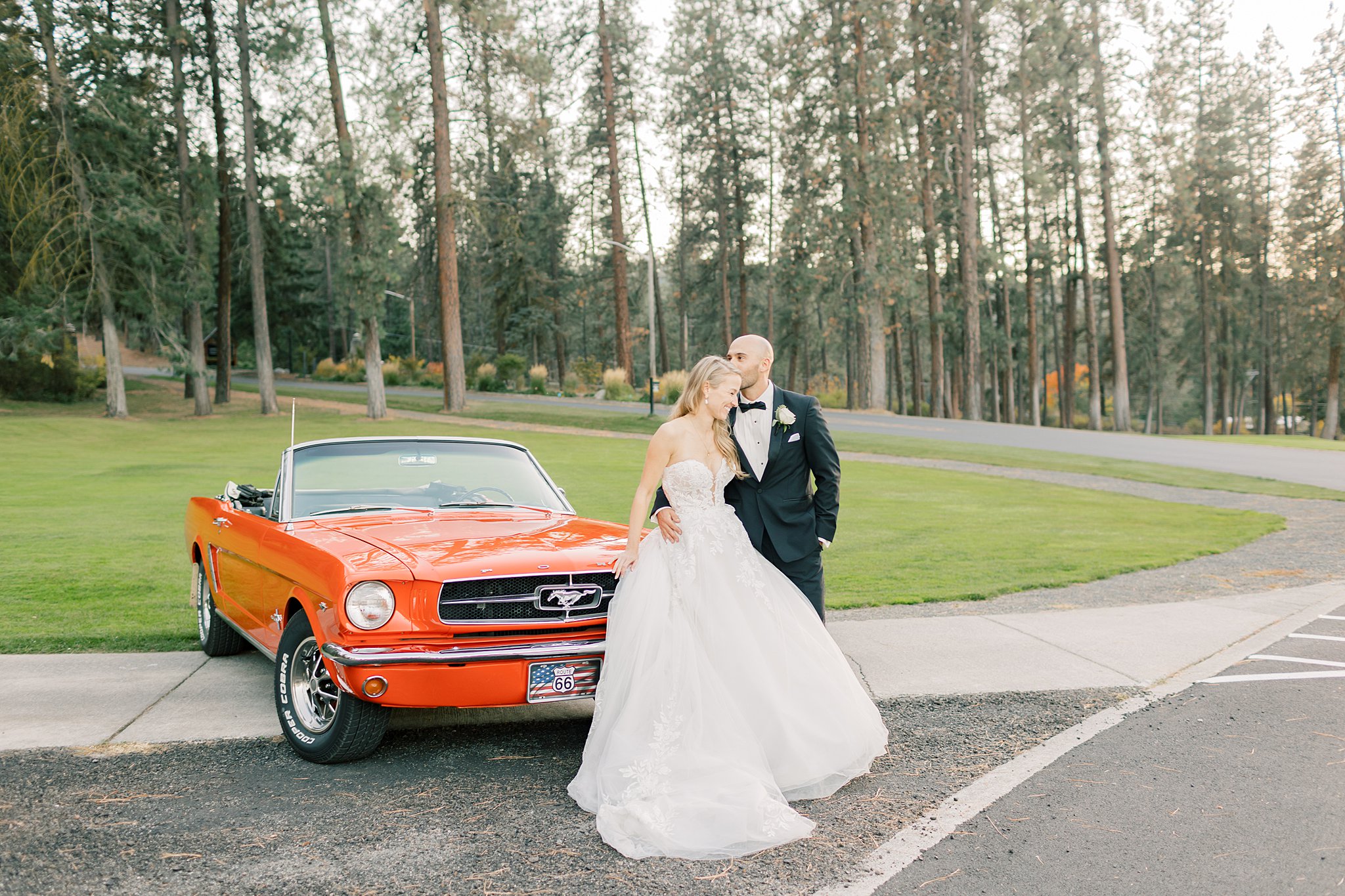 Newlyweds snuggle while leaning against a vintage orange Ford Mustang convertible at their Kalispel Country Club Wedding