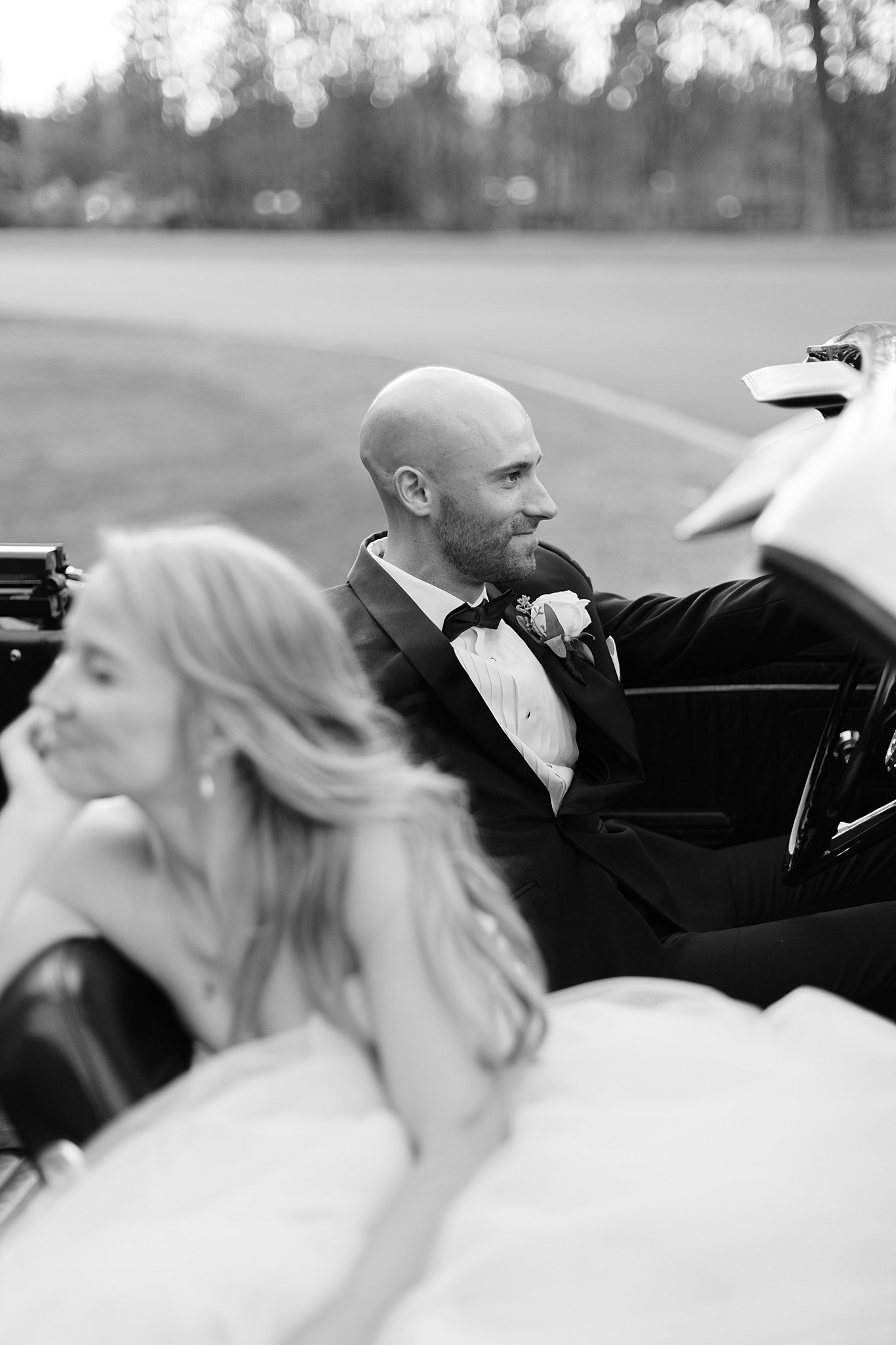 A black and white image of a bride and groom sitting in a vintage convertable