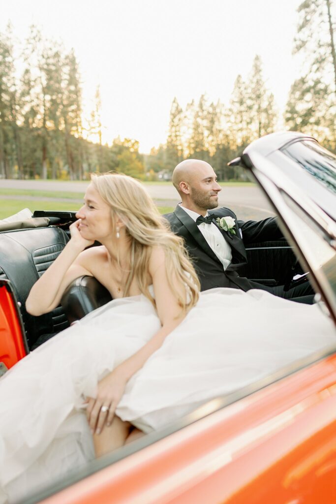 Newlyweds sit in the front seats of an orange Ford Mustang at sunset at their Kalispel Country Club Wedding