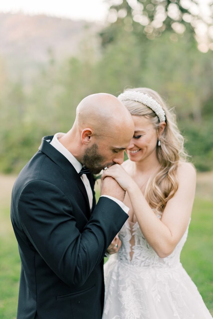 A groom kisses the hand of his smiling bride as they walk in a field at sunset