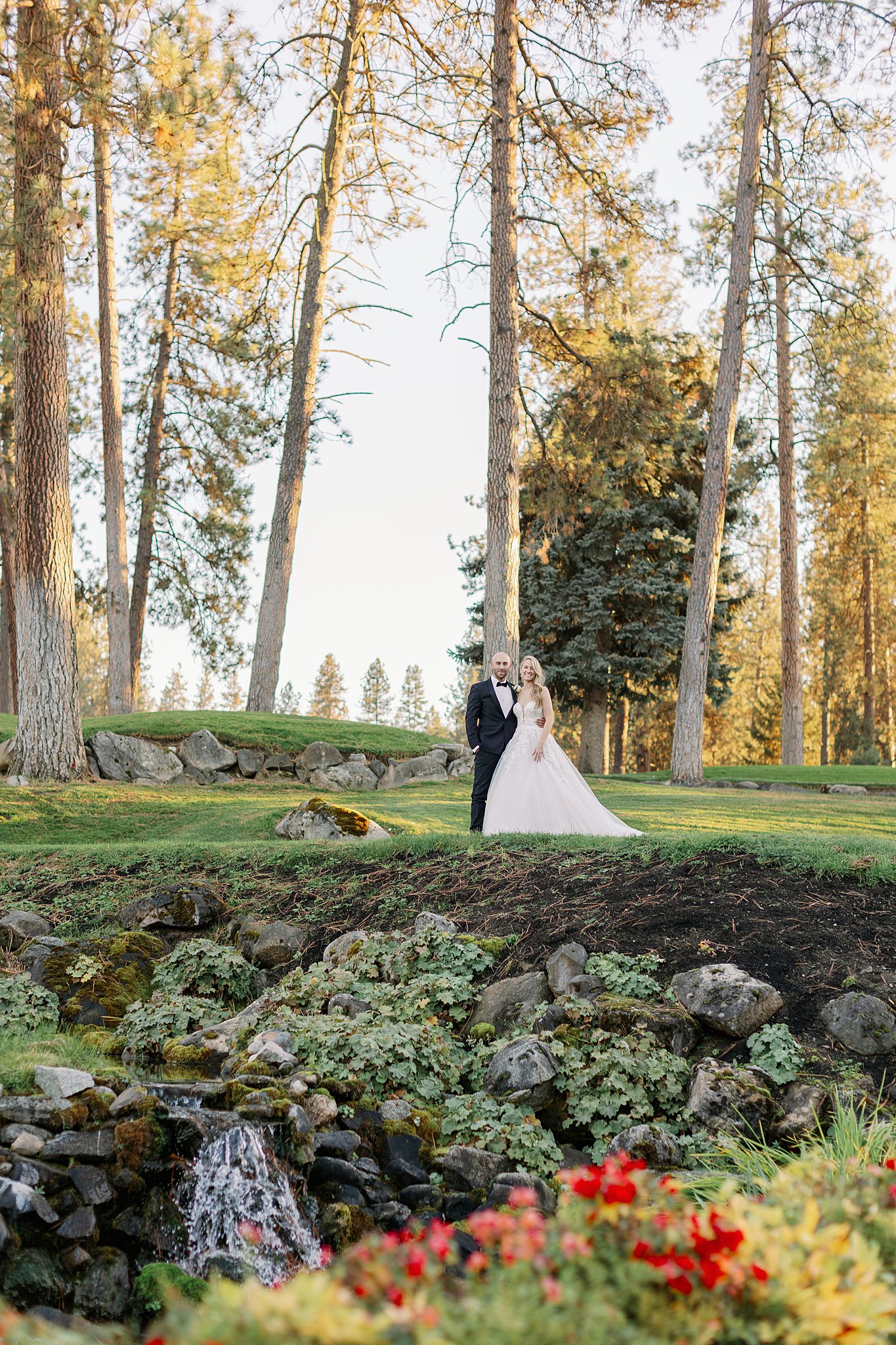 Newlyweds smile while watching a small waterfall in a garden at susnet