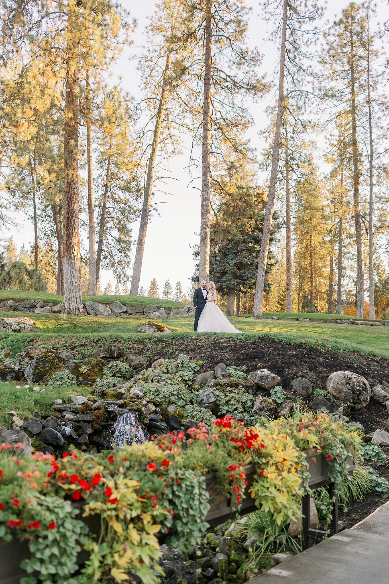 A bride and groom stand together in a garden with arms around each other at sunset at the Kalispel Country Club Wedding venue