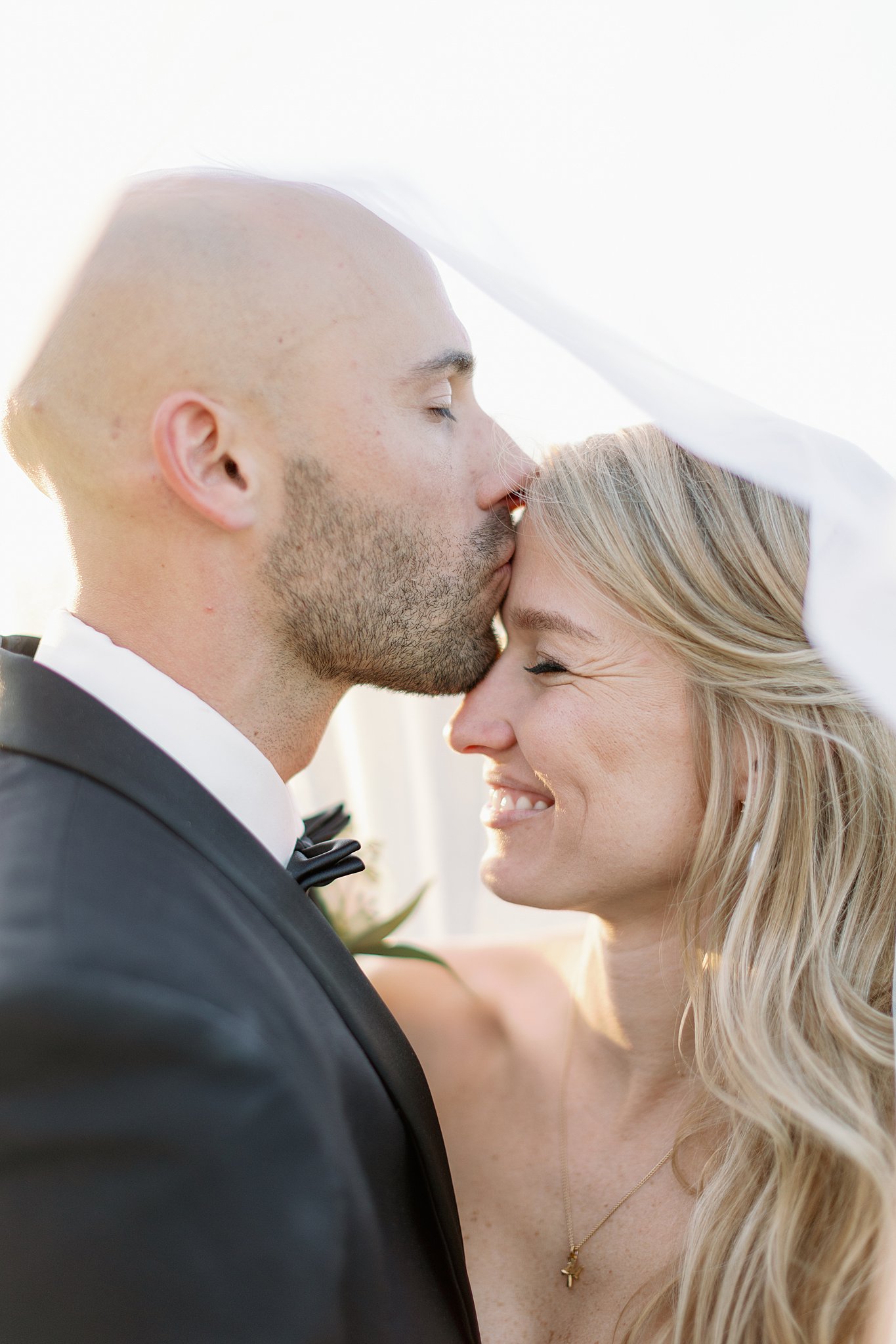 Newlyweds giggle and kiss under the veil at sunset