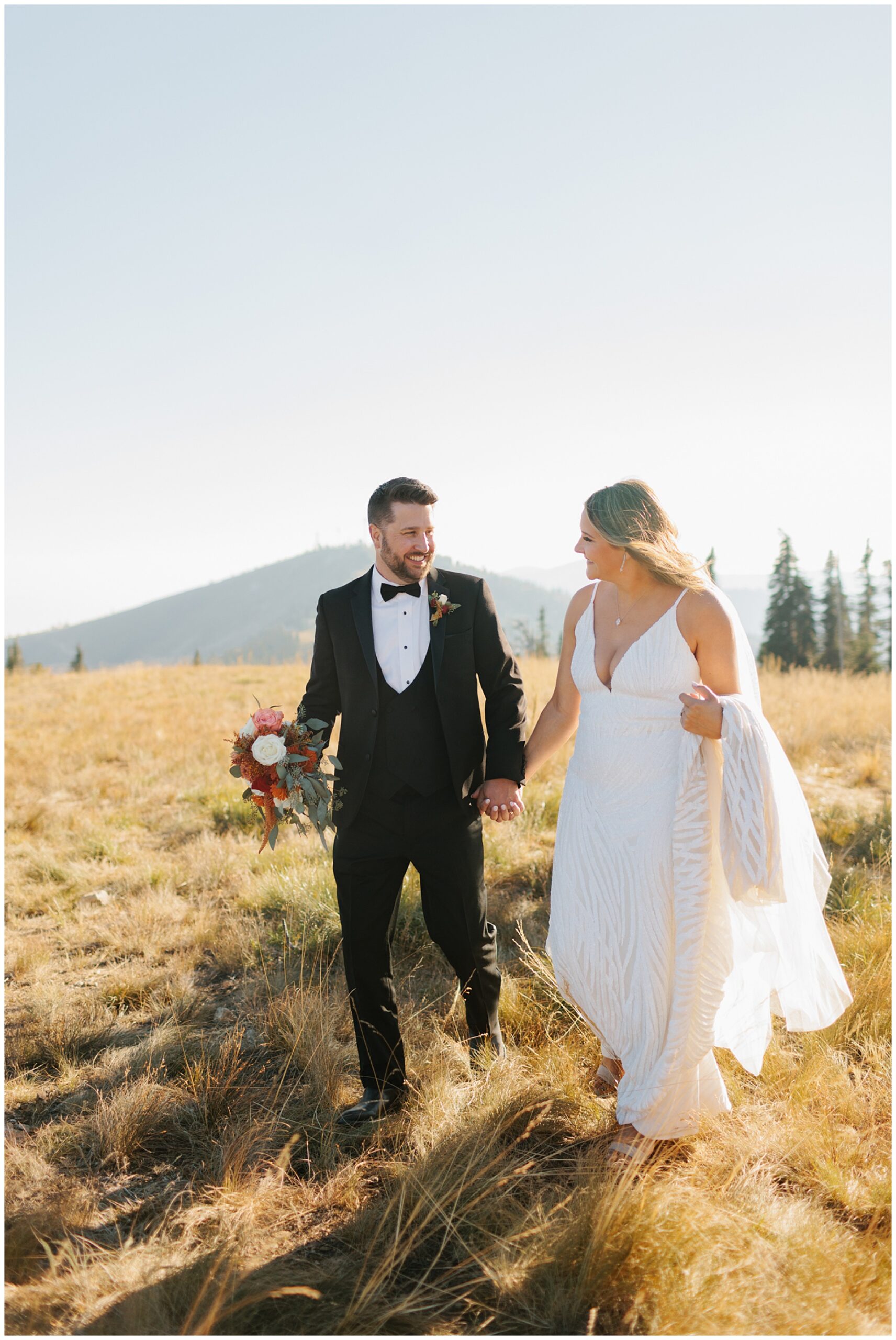 Newlyweds hold hands while walking in an open meadow on a mountain at their Schweitzer Mountain Wedding