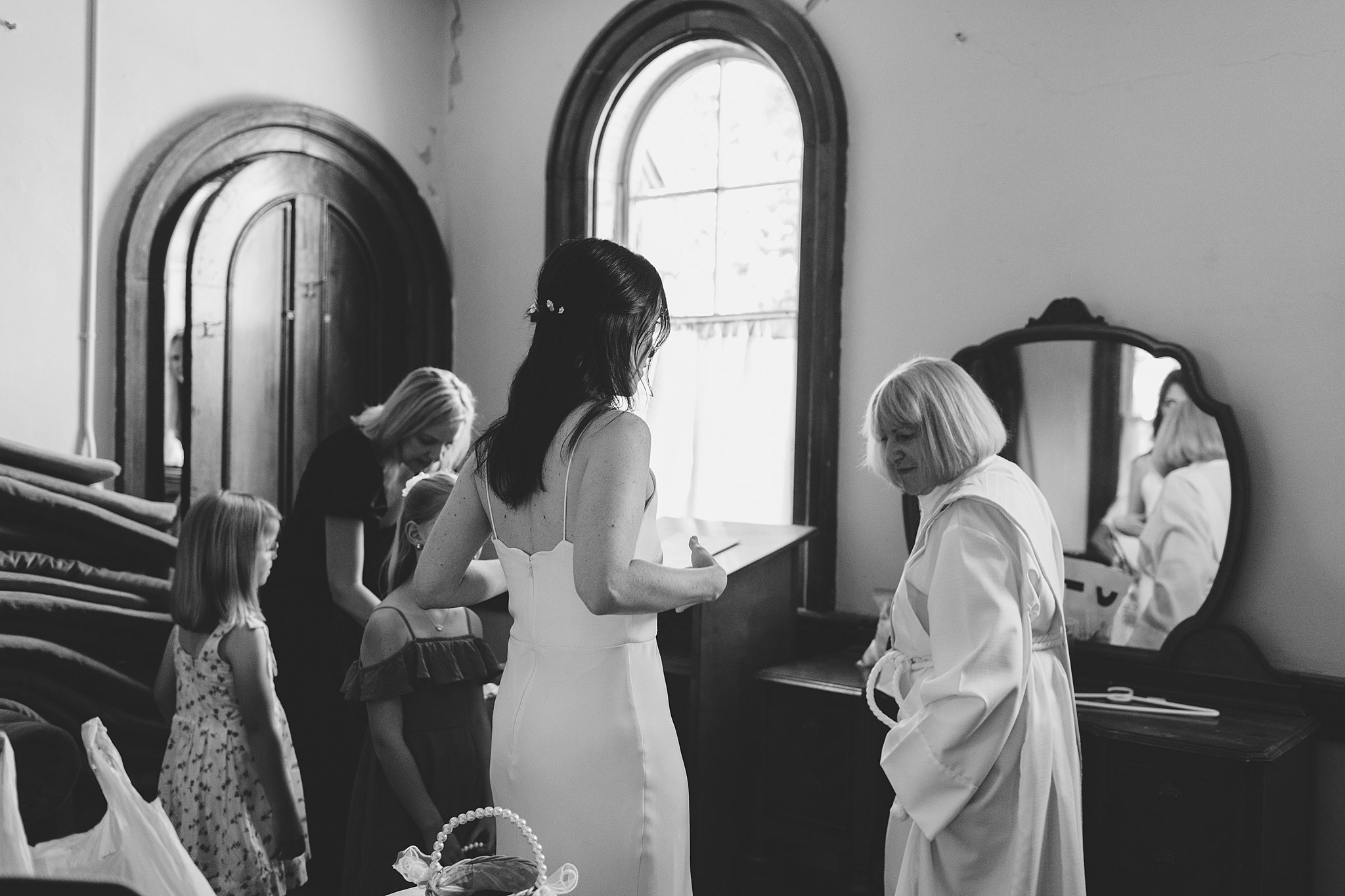 A bride chats with the officiant in the getting ready room with young girls at the fort sherman chapel