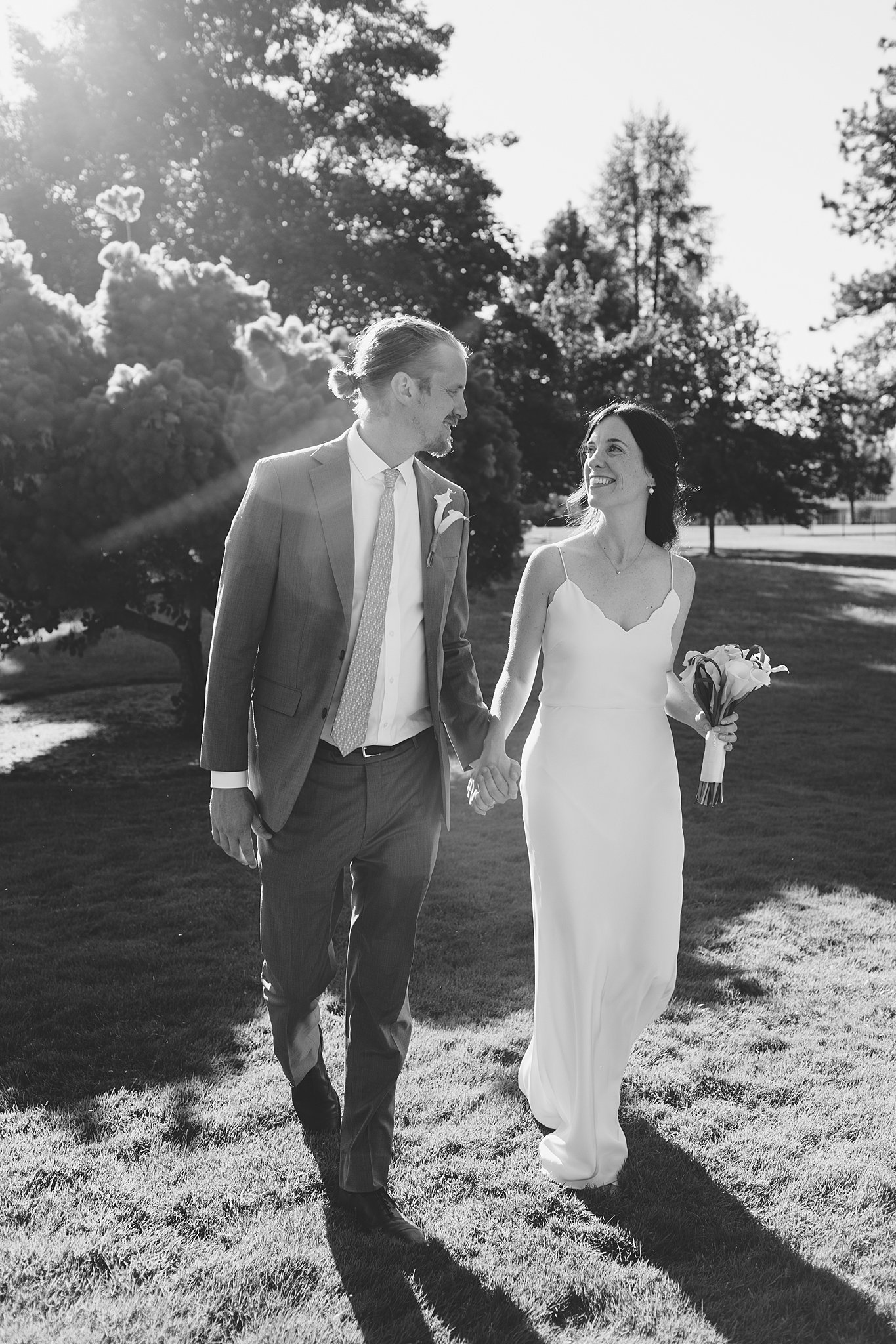 Newlyweds walk in the lawn holding hands and smiling at each other after their fort sherman chapel wedding ceremony