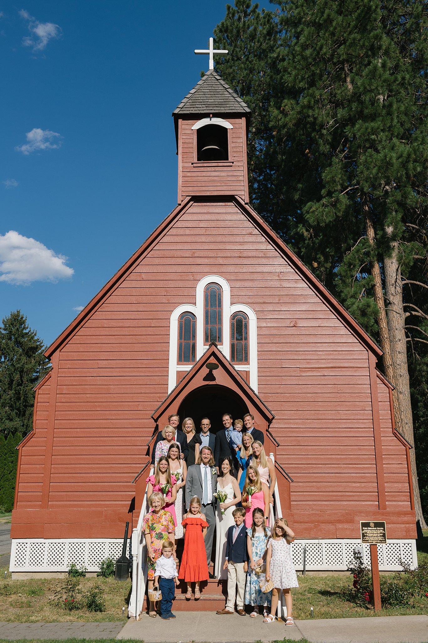 A bride and groom stand on the steps of the fort sherman chapel with their wedding guests smiling