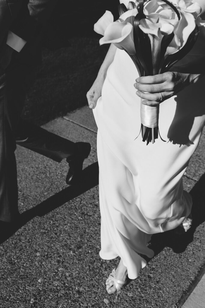 Details of a bride walking on a sidewalk holding a bouquet